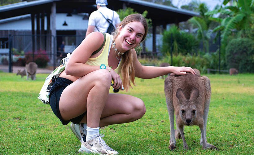 Student smiling crouched down next to kangaroo