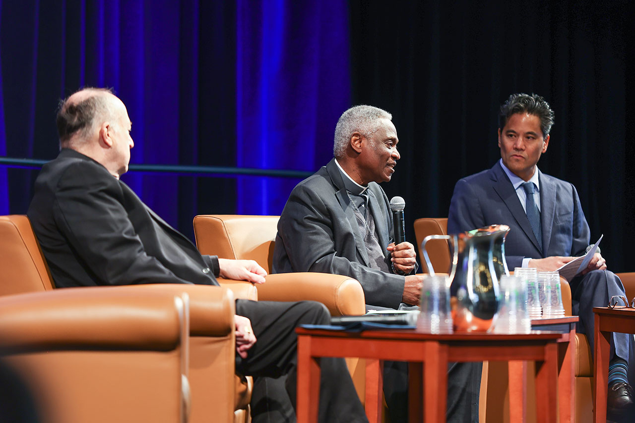 an Anti-Poverty Symposium panel features three men seated in leather chairs